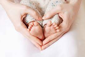 A baby's feet surrounded by their mothers hands in the shape of a heart